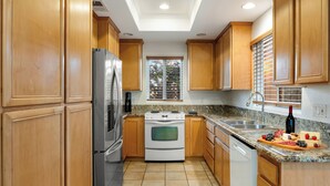 A kitchen with wooden cabinets, a stainless steel refrigerator, a white stove, and a granite countertop.