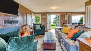 A cozy living room with a brick fireplace, comfortable seating, and a view of the outdoors. - Maxwelton Aerie | Bluffside Retreat w/ Sweeping Puget Sound Views + Firepit (Clinton)