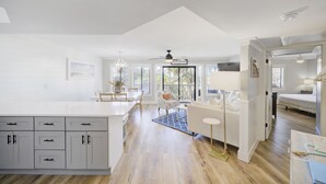 A spacious kitchen with a large island, a dining area with a chandelier, and a living room with a sofa and a lamp.