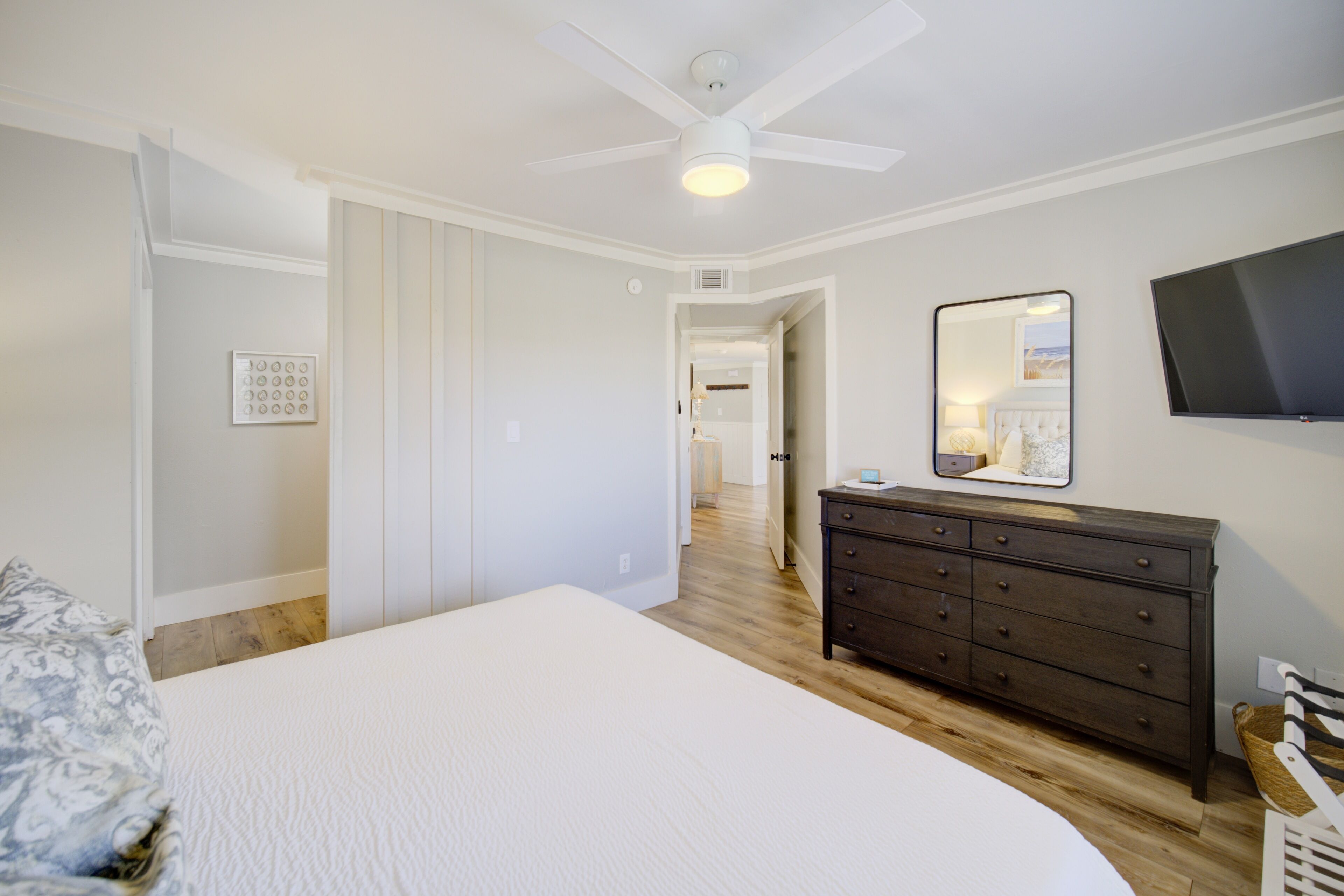 Ein Schlafzimmer mit Bett, Kommode, Spiegel und Deckenventilator.