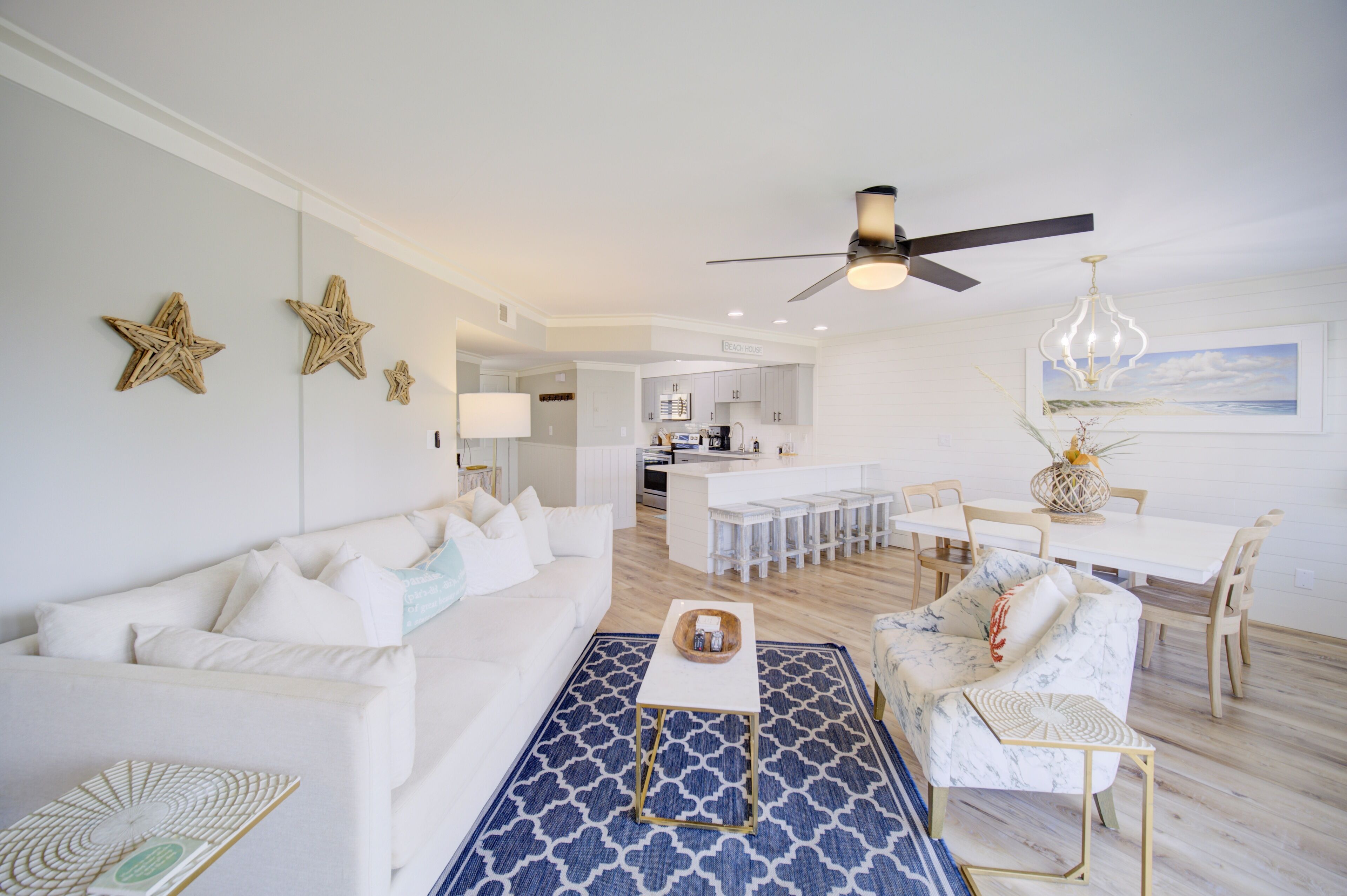 A modern living room with a white sofa, a blue patterned rug, and a dining area with a white table and chairs.