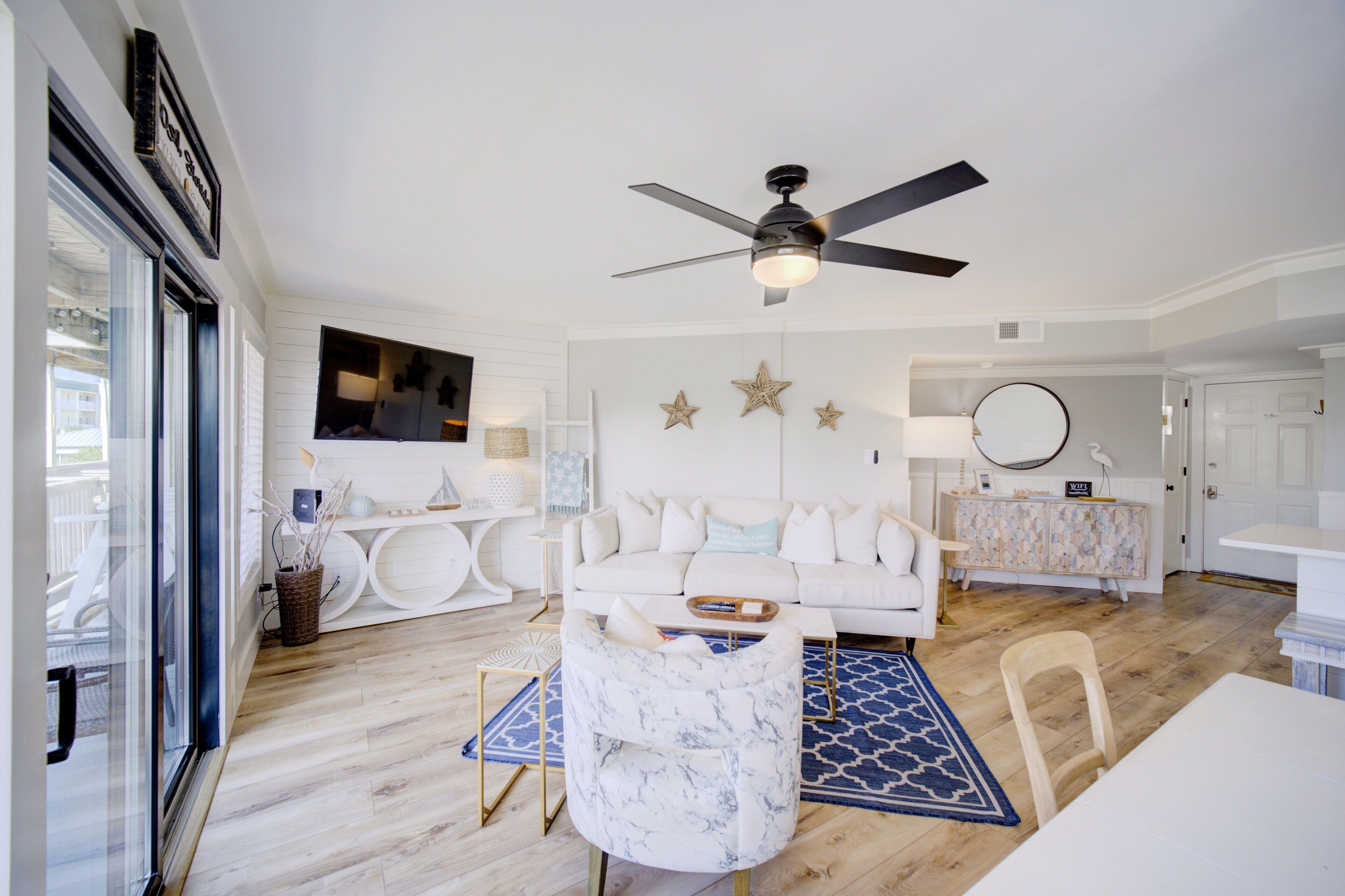 Ein modernes Wohnzimmer mit einem weißen Sofa, einem Marmorsessel, einem Deckenventilator und Holzboden.