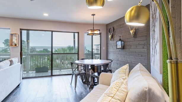 A modern living room with a round dining table, comfortable seating, and a view through large glass doors to an outdoor area.