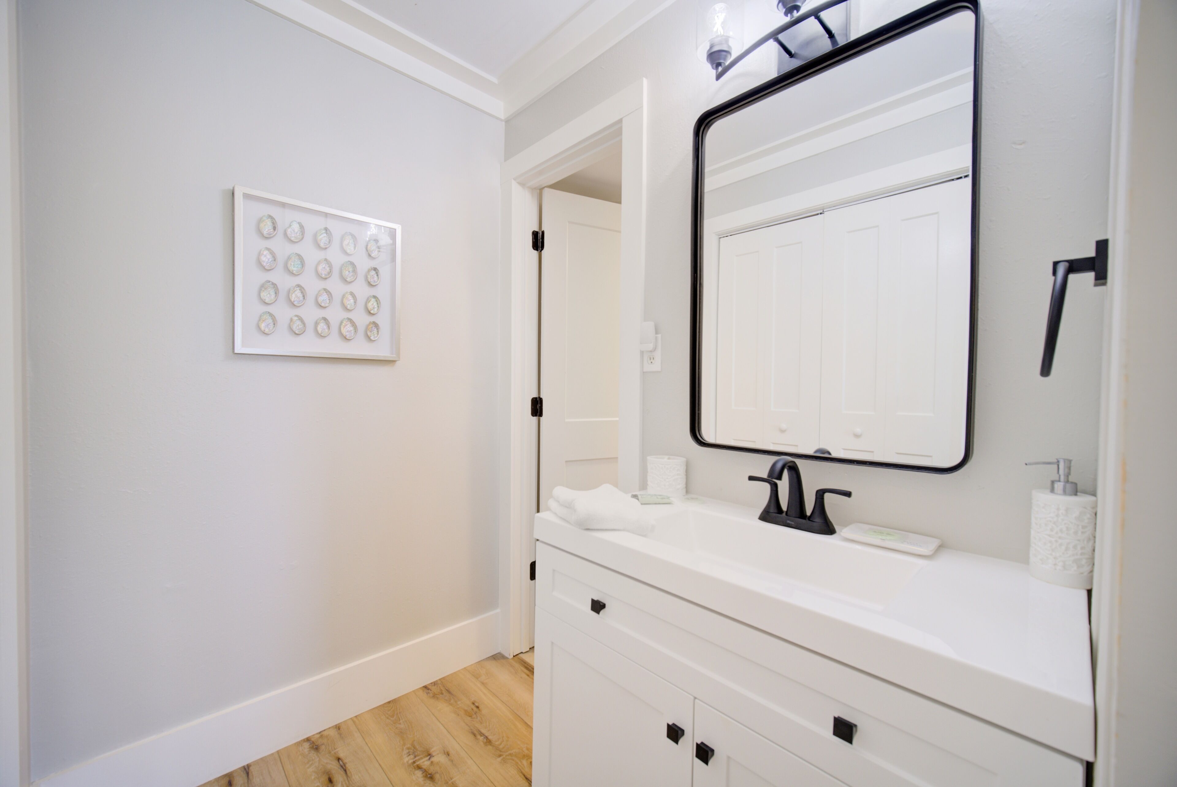 A bathroom with a white vanity, a large mirror, and a wall-mounted light fixture.