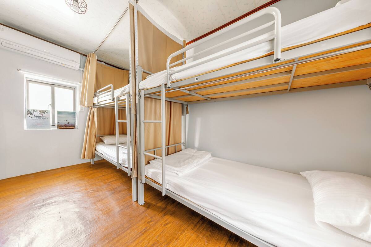 A bunk bed room with wooden flooring, a window with a view, and a curtain.