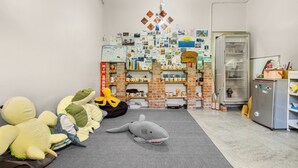 Habitación con alfombra gris, un refrigerador y una pared de ladrillo con estantes que contienen varios objetos.