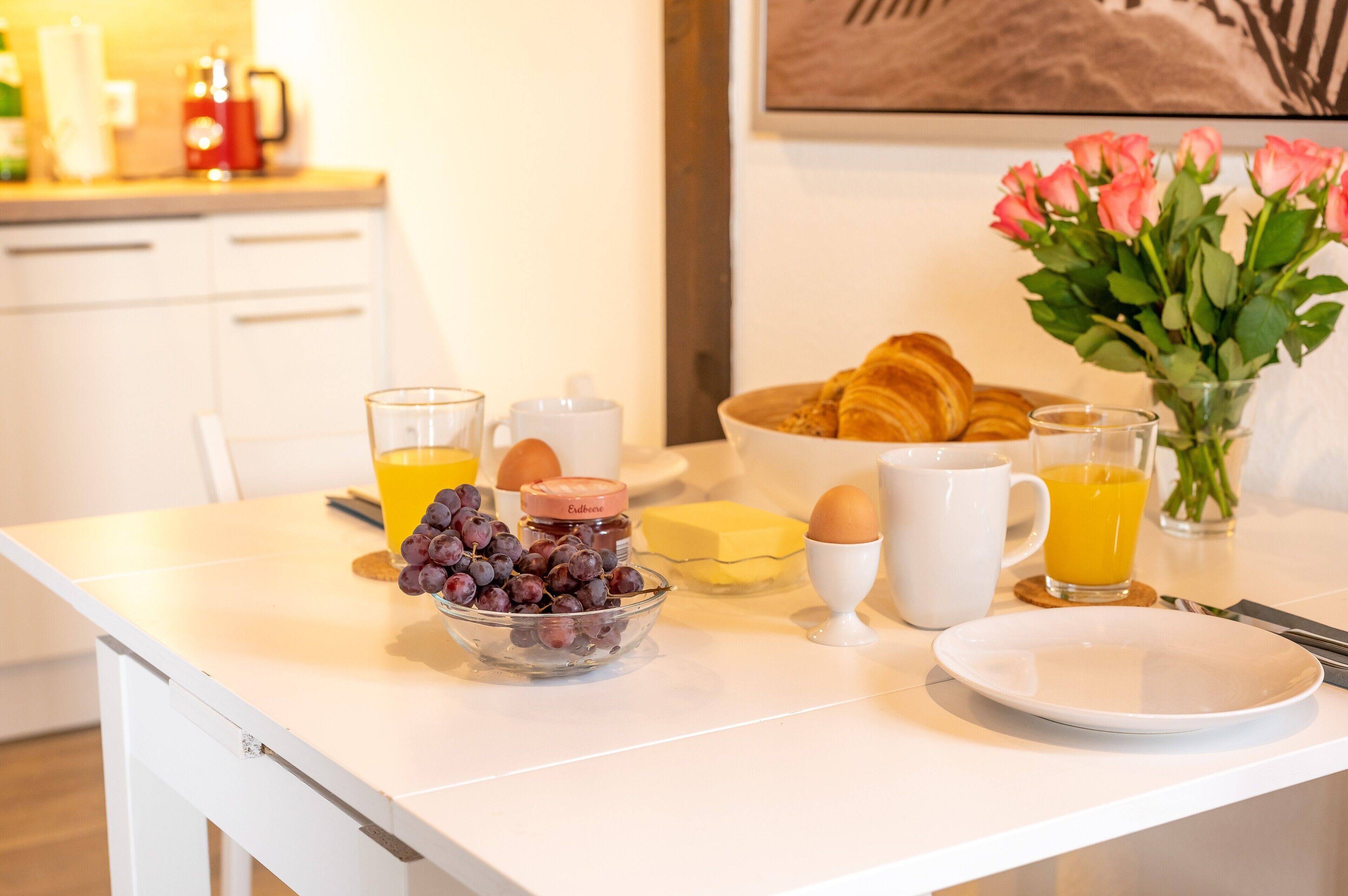 Ein Frühstücksbuffet mit Croissants, Eiern und einer Schale Trauben auf einem weißen Tisch.