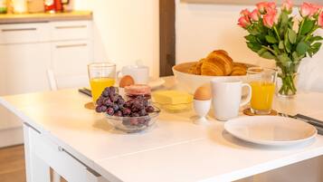 Ein Frühstücksbuffet mit Croissants, Eiern und einer Schale Trauben auf einem weißen Tisch.