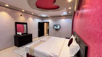 A modern bedroom with a large bed, a TV mounted on the wall, and a red accent wall.