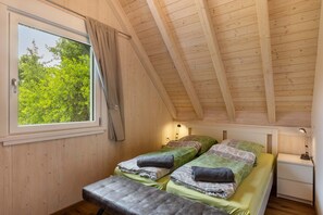 Una habitación pequeña con paneles de madera, dos camas, una ventana y una mesita de noche.