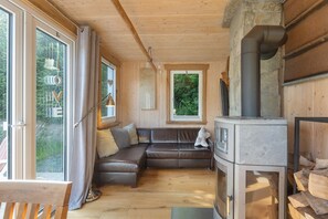 Un intérieur de chalet chaleureux avec un plancher en bois, un canapé en cuir, une cheminée et de grandes fenêtres.