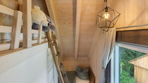A wooden interior with a loft bed, a ladder, a hanging light fixture, and a window with a view of greenery. - Holiday Home 'Ferienhaus Alpenzauber' with Mountain View, Private Terrace and Wi-Fi (Lennestadt)