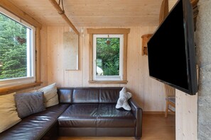 L’intérieur d’un chalet en bois est aménagé avec un canapé en cuir, un téléviseur et une fenêtre donnant sur un paysage verdoyant.