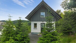 A modern house with a sloped roof, a small entrance, and surrounded by lush greenery. - Holiday Home 'Ferienhaus Alpenzauber' with Mountain View, Private Terrace and Wi-Fi (Lennestadt)