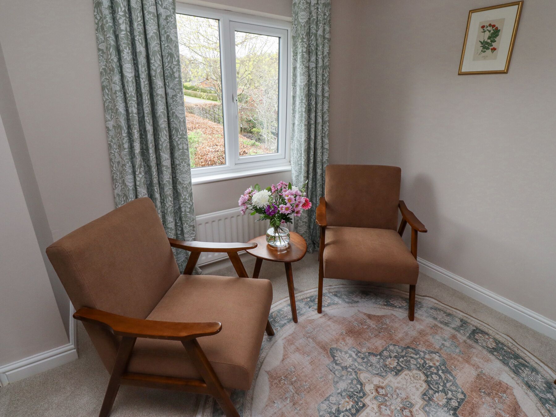 Une pièce avec deux fauteuils marron, une petite table ronde ornée d’un vase de fleurs et un tapis à motifs.
