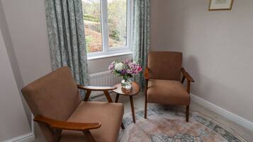 Une pièce avec deux fauteuils marron, une petite table ronde ornée d’un vase de fleurs et un tapis à motifs.