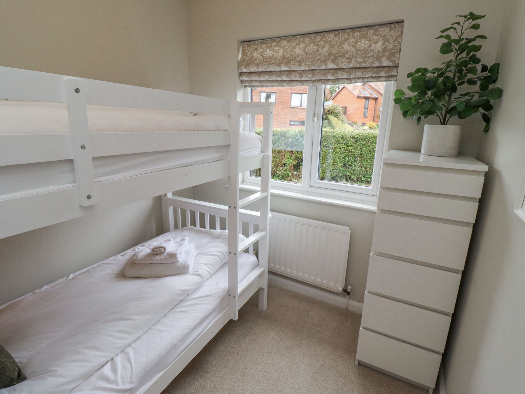 A bunk bed with a white headboard, a radiator below the window, and a plant on a white dresser.