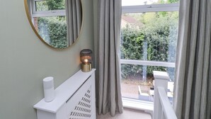 A bathroom with a white vanity, a round mirror, and a window with curtains. - Sparrow House (Alnwick)