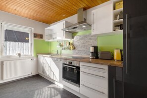 A modern kitchen with white cabinetry, a Bosch oven, a black refrigerator, and a window with a curtain.