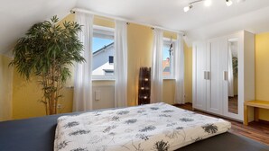 Un dormitorio con cama, una planta, un armario y una ventana con cortinas.