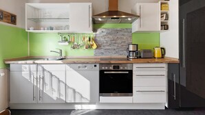 Una cocina moderna con armarios blancos, lavavajillas Bosch, horno empotrado y salpicadero de piedra.
