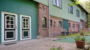 Un edificio con dos puertas de marco blanco, una sección de ladrillo y fachada verde.