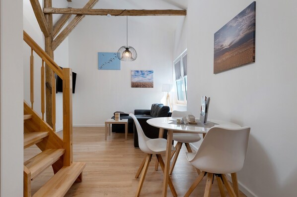 A modern interior with a staircase, wooden floors, a dining area with white chairs, a black sofa, and artwork on the walls.