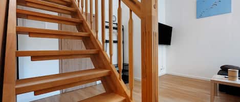 A wooden staircase with a modern design, a flat-screen TV mounted on the wall, and a wooden floor.