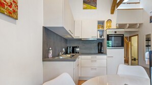 Kompakti keittiö, jossa on valkoiset kaapit, sisäänrakennettu uuni sekä ruokailutila pöydän ja tuolien kera.