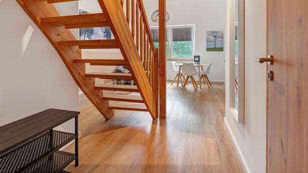Un escalier en bois mène à un espace repas comprenant une table et des chaises, un banc et une porte.
