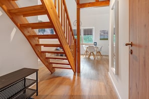 A wooden staircase leading to a dining area with a table and chairs, a bench, and a door.