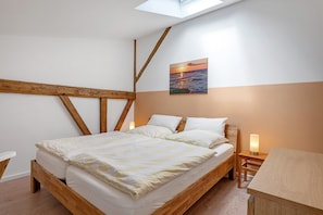 A room with a wooden bed, a bedside table with a lamp, a painting of a sunset, and a skylight.