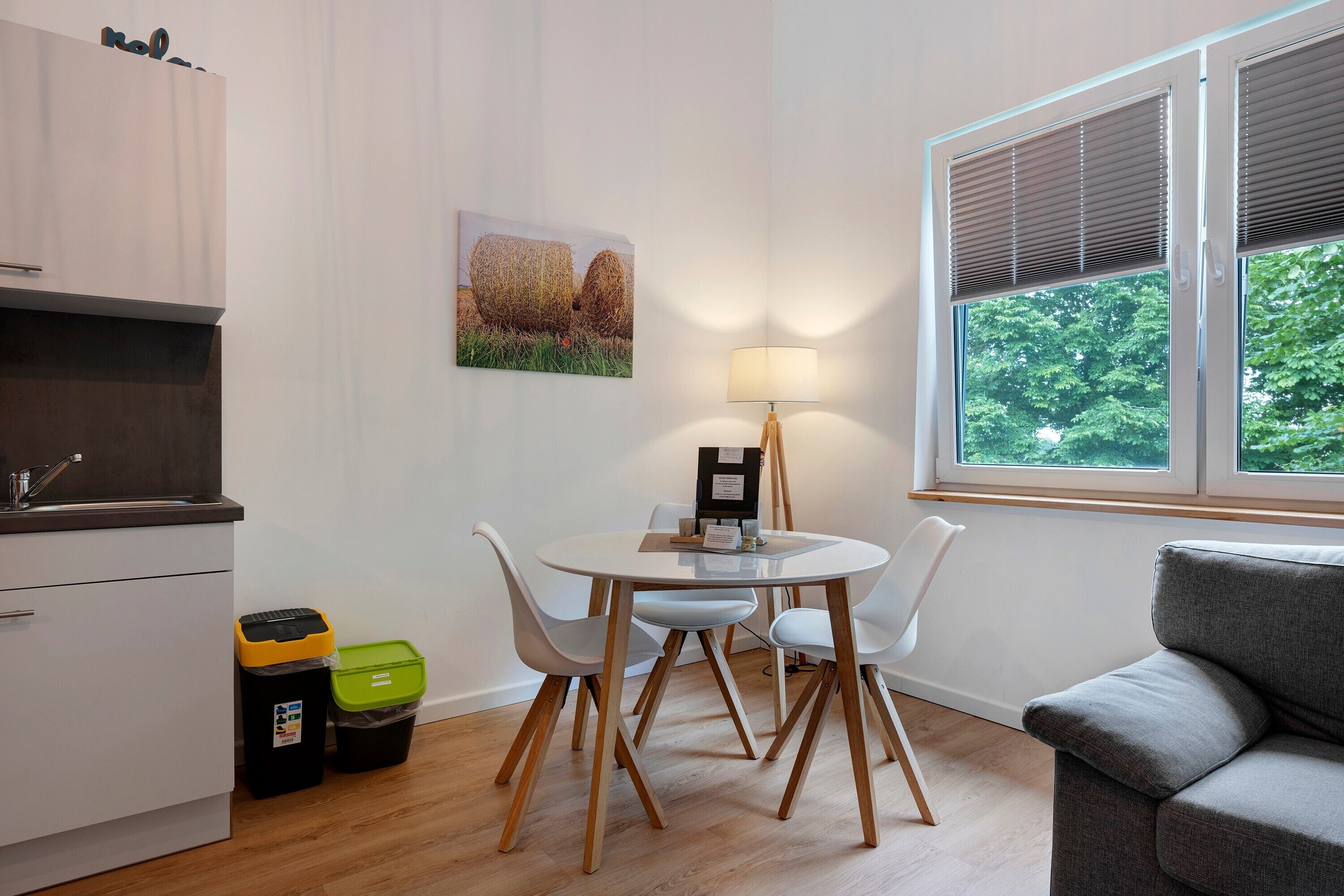 A modern kitchen with white cabinets, a dining table with chairs, a lamp, and a window with blinds.