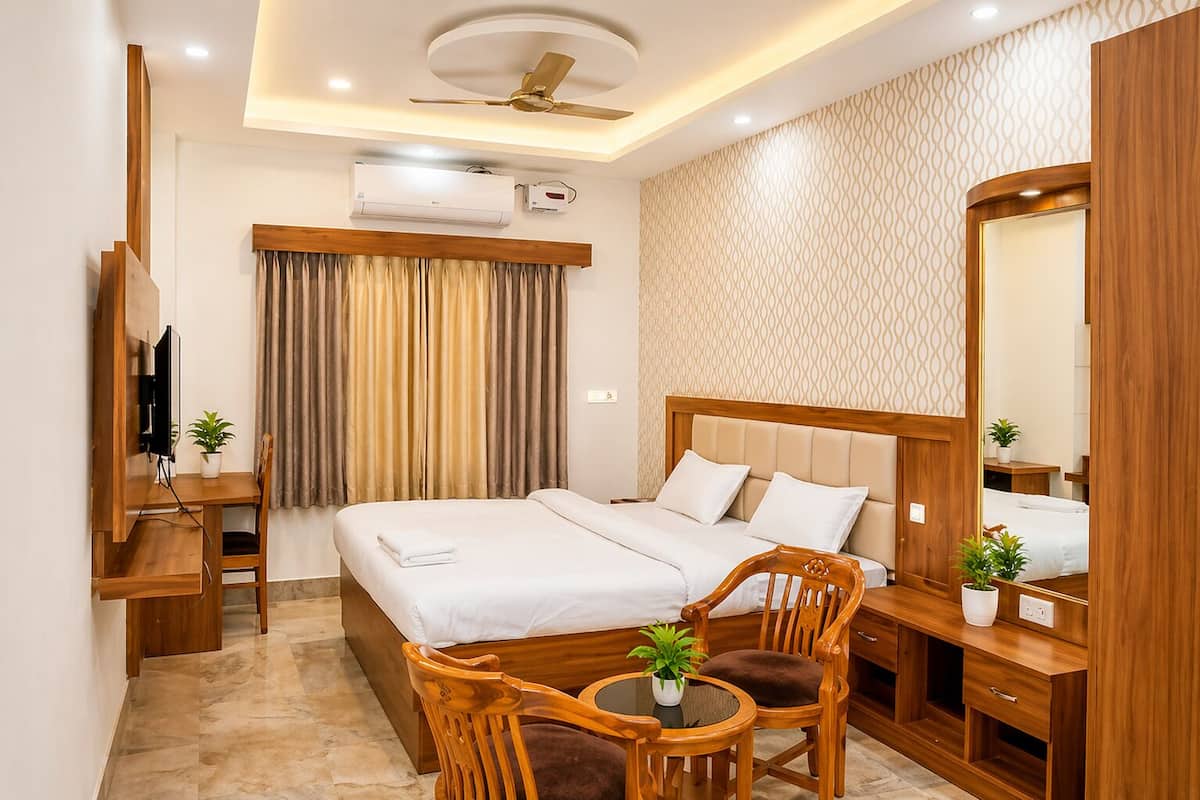 A hotel room with a bed, a desk, a chair, a small table, a ceiling fan, an air conditioning unit, and a mirror.