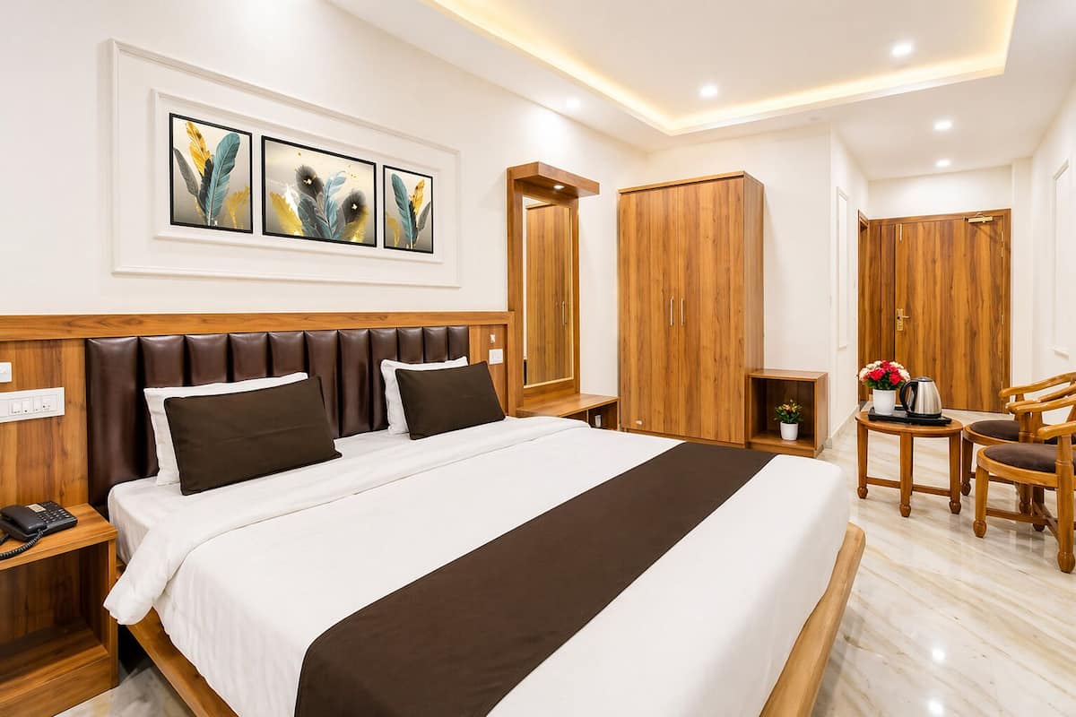 A hotel room with a large bed, wooden headboard, a desk with a chair, a wardrobe, and artwork on the wall.