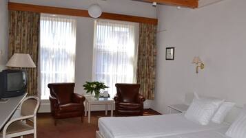 Relax in a serene space with a large bed, desk, and comfortable armchairs.