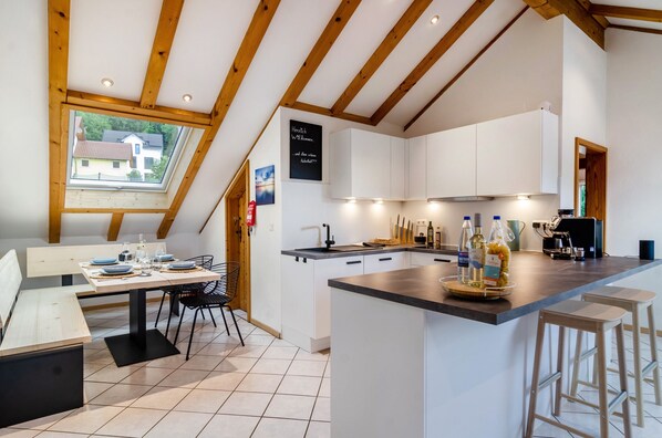 A modern kitchen with white cabinets, a wooden ceiling, and a dining area with a table and chairs. - Apartment 'Enjoy Mal' with Shared Garden, Balcony and Wi-Fi (Stockach)