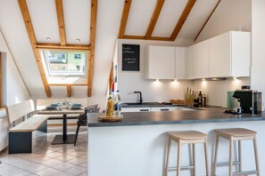 Une cuisine moderne avec des meubles blancs, un plafond en bois et un coin repas comprenant un banc et une table.