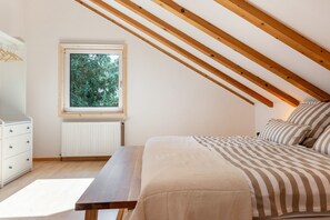 A bedroom with a sloped ceiling, a window with a view of trees, a bed with striped bedding, a bedside table, and a dresser. - Apartment 'Enjoy Mal' with Shared Garden, Balcony and Wi-Fi (Stockach)