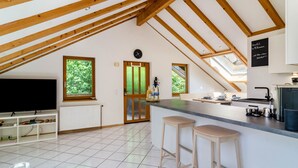 Una cocina moderna con una isla central, vigas de madera, un ventanal grande y un reloj en la pared.
