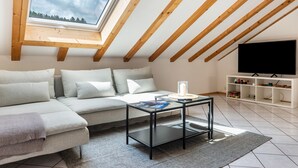 Una sala de estar moderna con techo inclinado, un sofá, una mesa de centro, un televisor y una estantería.