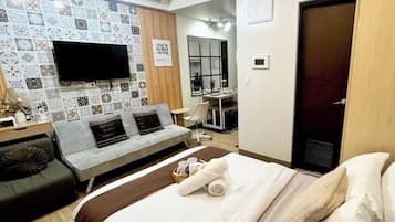 A hotel room with a bed, a sofa, a TV mounted on the wall, and a desk with a chair.
