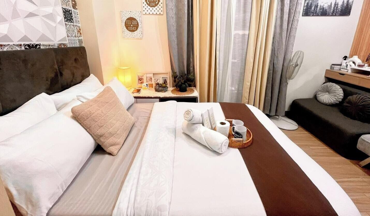 A hotel room with a bed, bedside table, curtains, and a sofa.