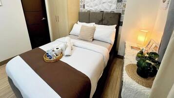 A hotel room with a bed, a bedside table with a lamp, a plant, and a tray with toiletries.