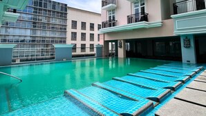 Una piscina con agua cristalina y azul, rodeada por un edificio de varios pisos con balcones.