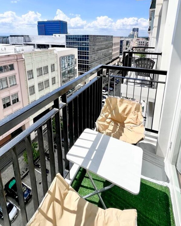 A balcony with a small table and chairs, a view of the cityscape, and a grassy area.