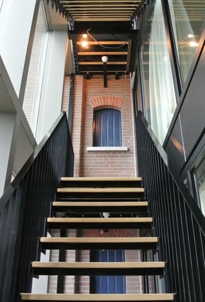 Stunning staircase with clean lines and a unique blend of wood tones, leading to a brick wall with a beautiful window.