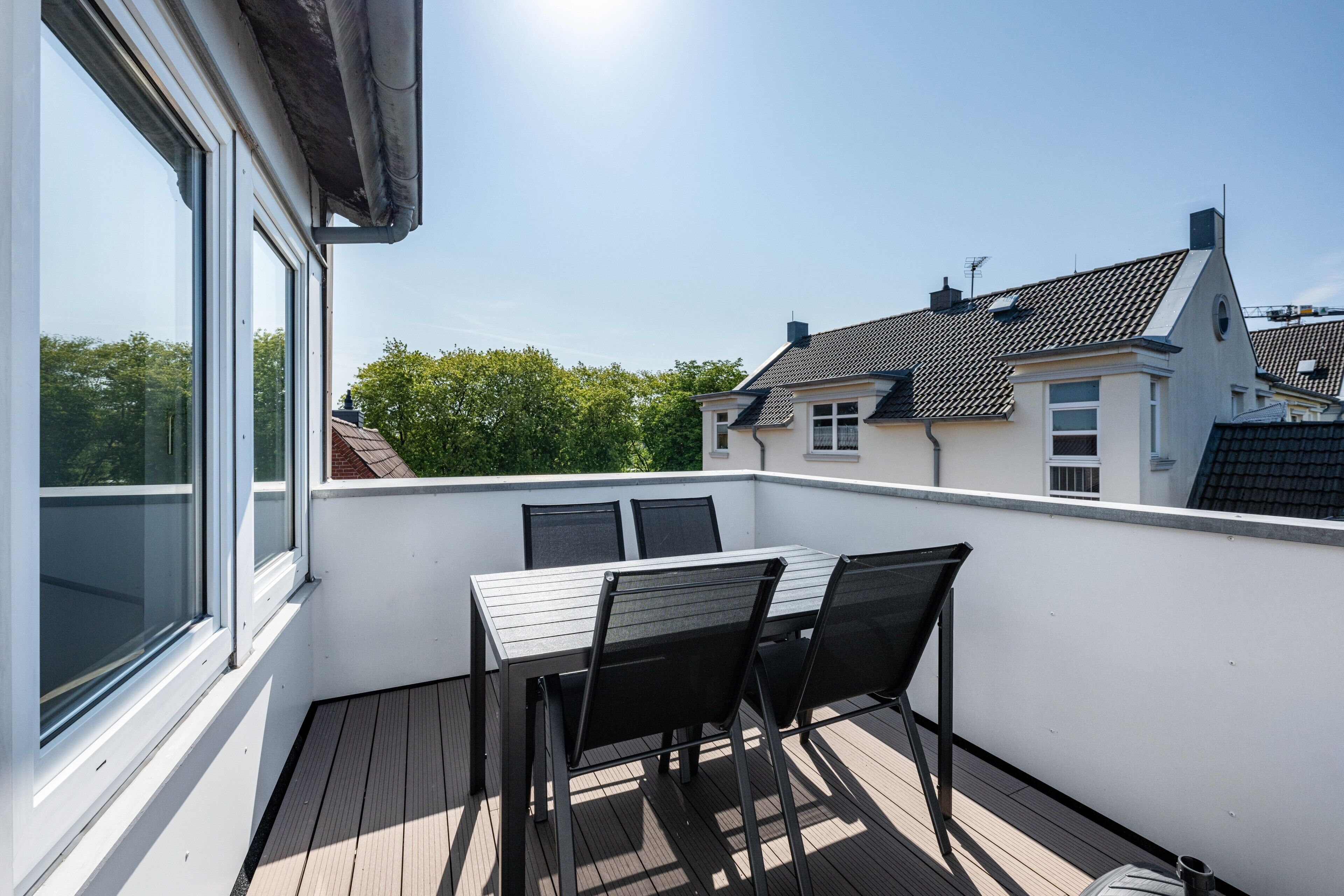 A balcony with a table and chairs, overlooking a residential area with houses and trees.