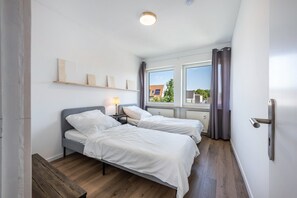 Una camera da letto con due letti, un comodino con una lampada, una panca di legno e una finestra con tende.