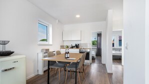 A modern kitchen with white cabinets, a dining table with chairs, a refrigerator, and a window with a view of greenery. - Apartment 'Mit Dachterrasse' with Lake View, Balcony and Wi-Fi (Heide)